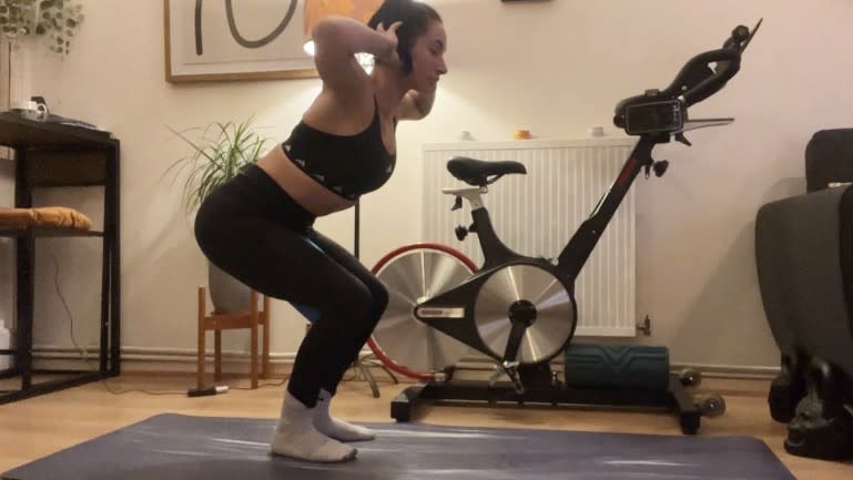 Sam performing prisoner squat on yoga mat with block between thighs