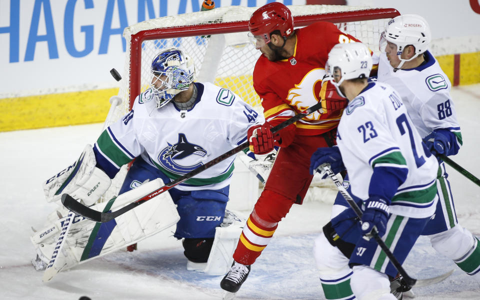 Vancouver Canucks goalie Braden Holtby, left, watchees the puck as Calgary Flames' Josh Leivo closes in during the first period of an NHL hockey game Saturday, Jan. 16, 2021, in Calgary, Alberta. (Jeff McIntosh/The Canadian Press via AP)