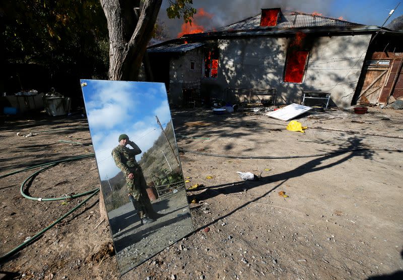 A man is reflected in a mirror as he stands near a house set on fire by departing Ethnic Armenians in the village of Cherektar, in the region of Nagorno-Karabakh