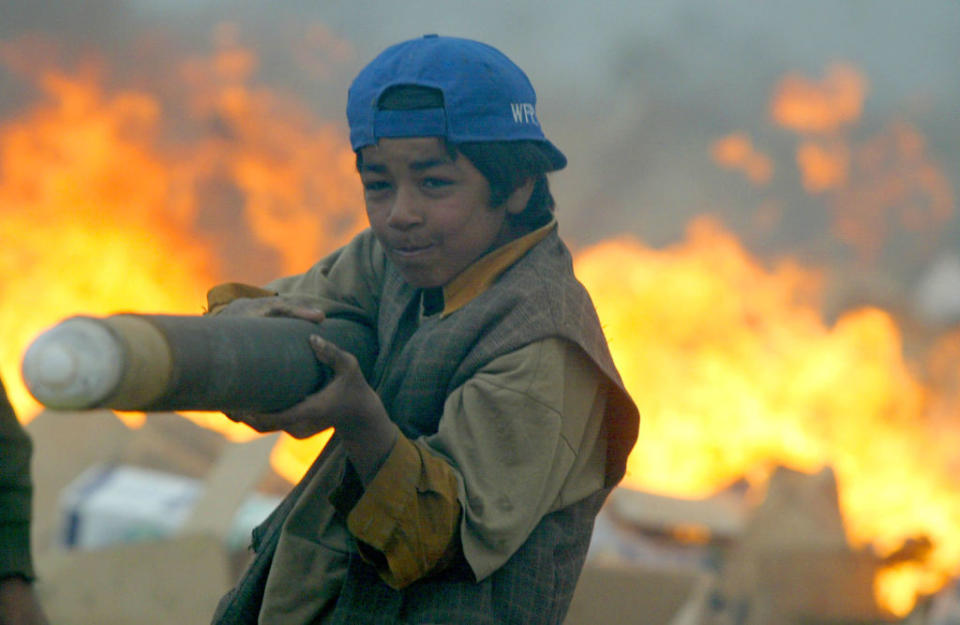 “I know the end of ‘Prime Time’ is coming,” says the Cardboard Lord, who upped NYC’s open-mic ante by reenacting the diversions of children in conflict zones. Here an Afghan child aims a makeshift bazooka fashioned from a carboard tube scavenged from the U.S. Air Force’s garbage dump at the since abandoned Bagram Air Base, site also of a detention facility under the now fallen U.S.-backed regime. (Credit: Joe Raedle/Getty Images)