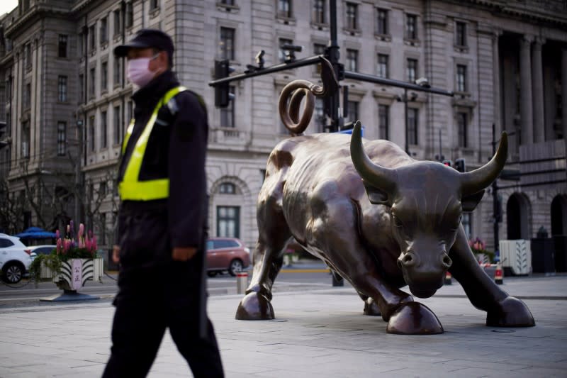 Un guardia de seguridad con una máscara pasa junto a una estatua del toro de Wall Street, luego del brote por la nueva enfermedad por coronavirus (COVID-19), en Shanghai, China