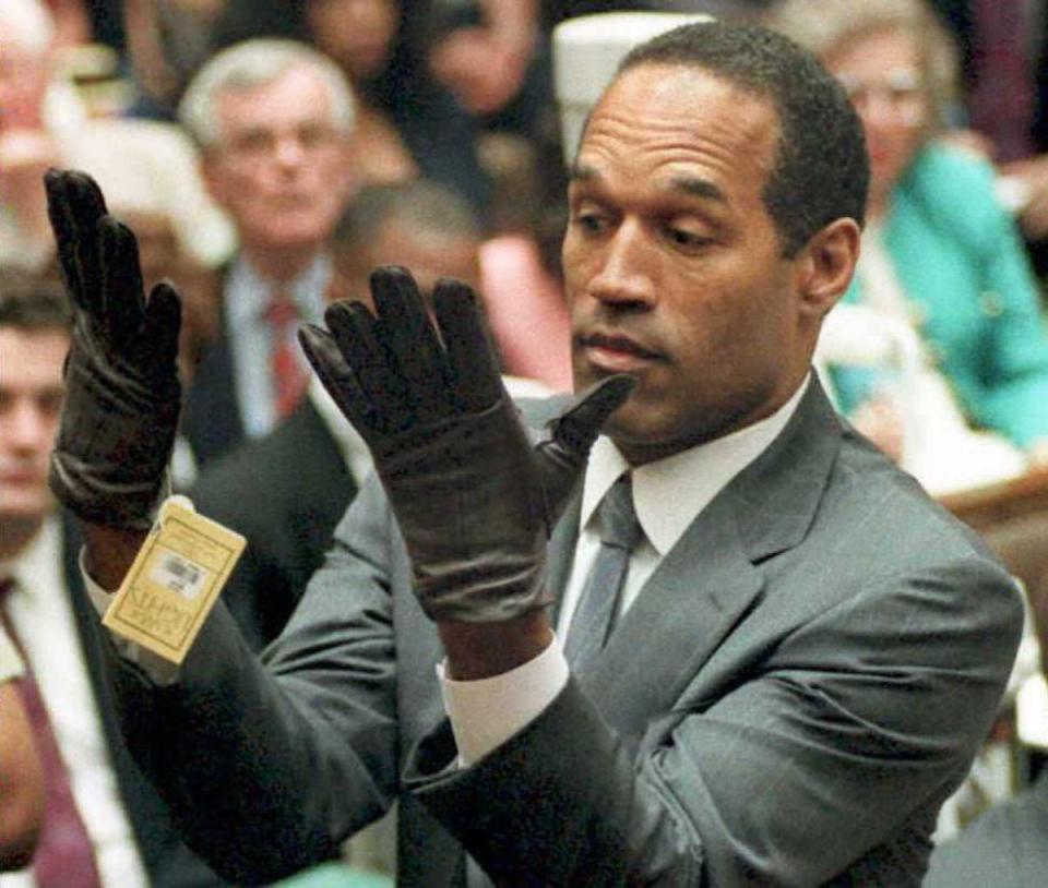 O. J. Simpson examina un par de guantes Aris que los fiscales le hicieron probar el 21 de junio de 1995 durante su juicio por doble asesinato en Los Ángeles. (AFP via Getty Images)