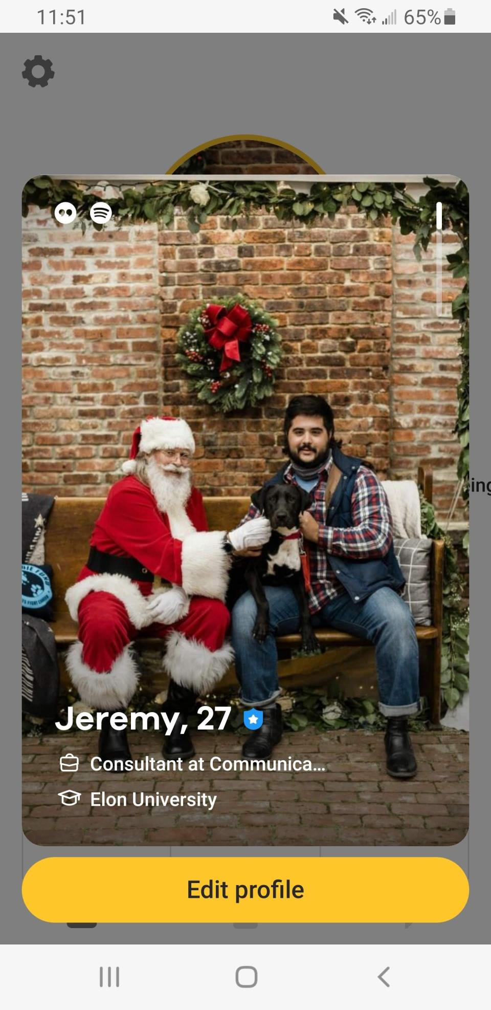A man dressed as Santa sits with a black dog and a man in plaid.