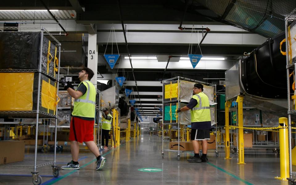 Amazon workers move containers to delivery trucks at an Amazon warehouse facility in Goodyear, Ariz. Starting Monday, Aug. 9, 2021, Amazon will be requiring all of its 900,000 U.S. warehouse workers to wear masks indoors, regardless of their vaccination status. The move follows steps by a slew of other retailers, including Walmart and Target, to mandate masks for their workers. In many of those cases the mandates apply to workers in locations of substantial COVID-19 transmission - AP