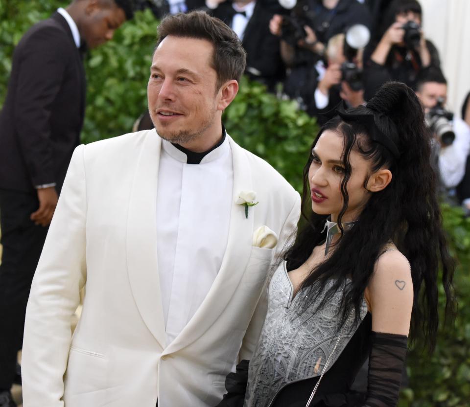 Elon Musk (left) and Grimes (right) standing next to each other and posing for photographers.