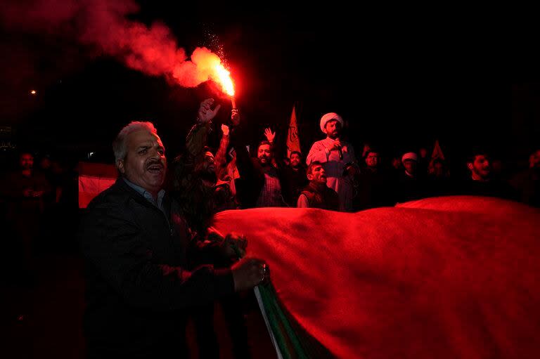 Un manifestante iraní enciende una bengala mientras otros portan una bandera palestina durante una reunión antiisraelí en la plaza Felestin (Palestina). en Teherán, Irán