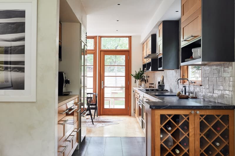 Warm kitchen with doors that open to a patio. Black countertops, warm wood cabinets with black details, and a built-in wine storage area.