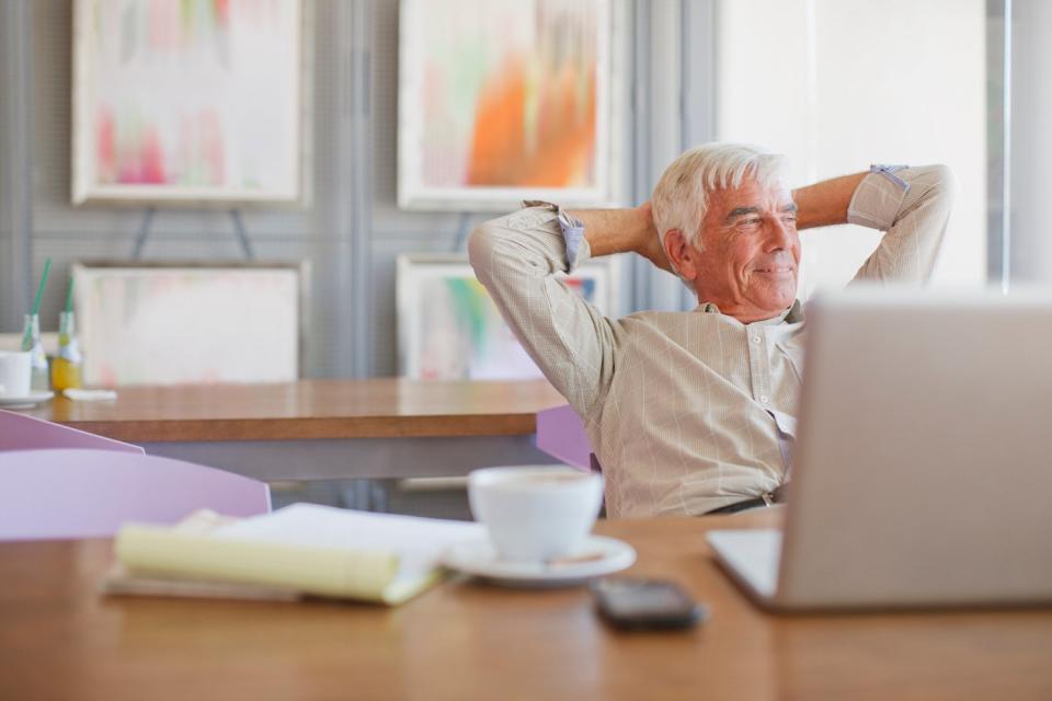 A smiling person with hands behind head sitting in front of a laptop.