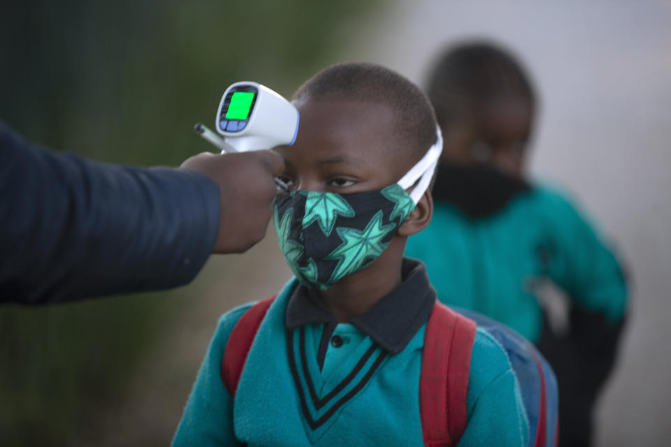 A pupil's temperature is checked on returning to school in Johannesburg, Tuesday July 7, 2020, as more learners were permitted to return to class. Schools were shut down in March prior to a total country lockdown in a bid to prevent the spread of coronavirus and are now slowly being re-opened. (AP Photo/Denis Farrell)