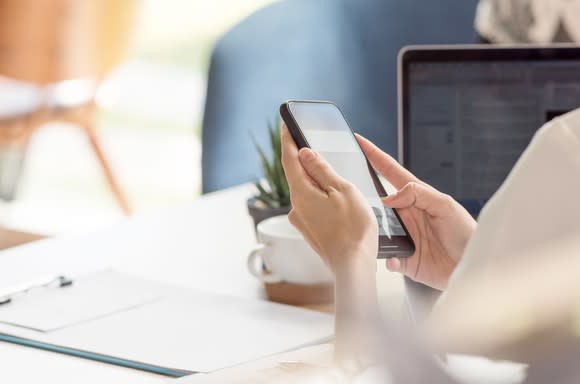 Hands holding a cell phone while sitting at a desk