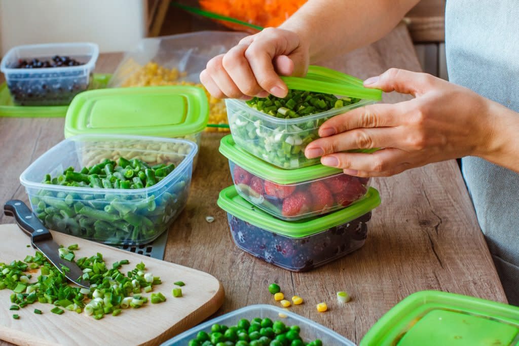 A woman meal preps by cutting up fruits and vegetables and placing them in Tupperware. 