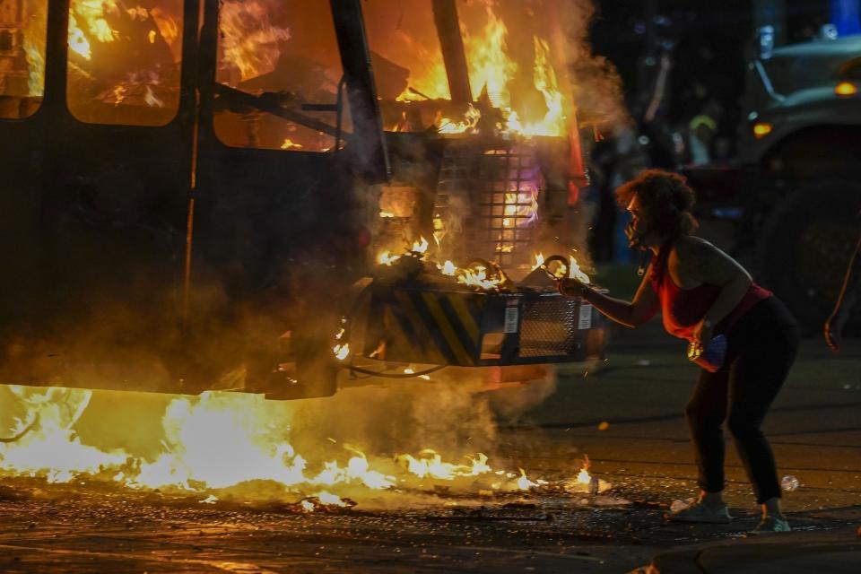 A protester lights a cigarette on a garbage truck that was set on fire during protests late Monday, Aug. 24, 2020, in Kenosha, Wis., sparked by the shooting of Jacob Blake by a Kenosha Police officer a day earlier. (AP Photo/Morry Gash)