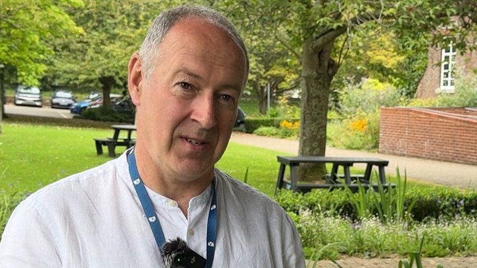 Nick Ireland in a white collarless shirt standing in front of the Public Gardens