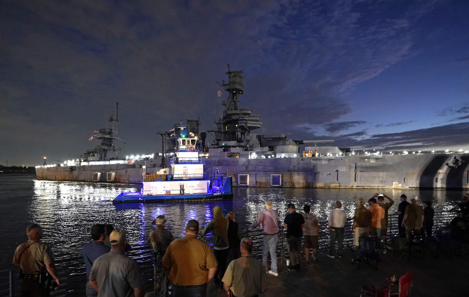 People watch as the USS Texas is moved from the dock Wednesday, Aug. 31, 2022, in La Porte, Texas. The vessel, which was commissioned in 1914 and served in both World War I and World War II, is being towed down the Houston Ship Channel to a dry dock in Galveston where it will undergo an extensive $35 million repair. (AP Photo/David J. Phillip)