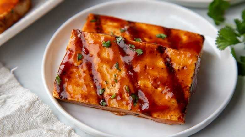 grilled bbq tofu slices on white plate with cilantro garnish