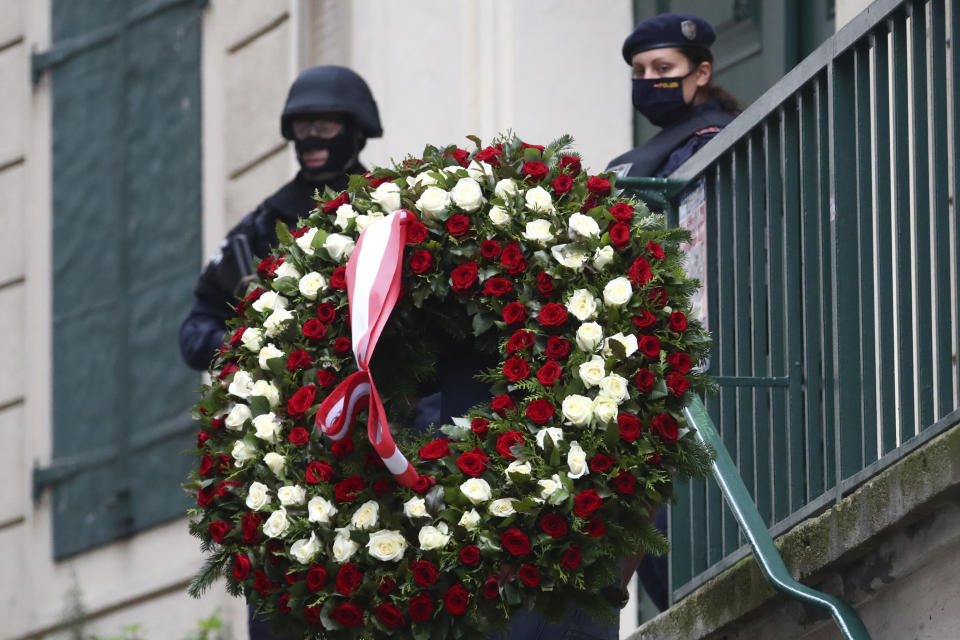 A man carries a wreath as he walks past police officers in Vienna, Austria, Tuesday, Nov. 3, 2020. Police in the Austrian capital said several shots were fired shortly after 8 p.m. local time on Monday, Nov. 2, in a lively street in the city center of Vienna. Austria's top security official said authorities believe there were several gunmen involved and that a police operation was still ongoing. (AP Photo/Matthias Schrader)