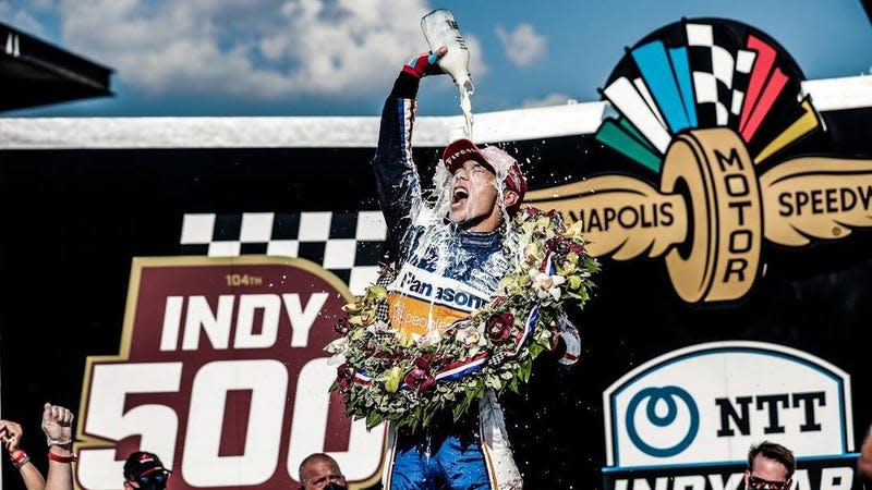 Japanese driver Takuma Sato celebrates his second victory at the 2020 Indianapolis Motor Speedway. He is pouring milk over his head while wearing the traditional winner's wreath.