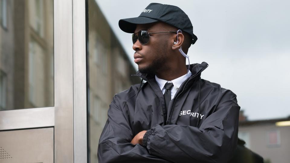 Portrait Of Young African Male Security Guard Standing Arms Crossed.