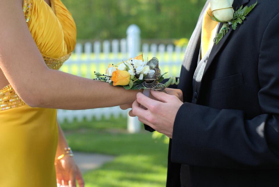 man placing flowers on woman's wrist for prom