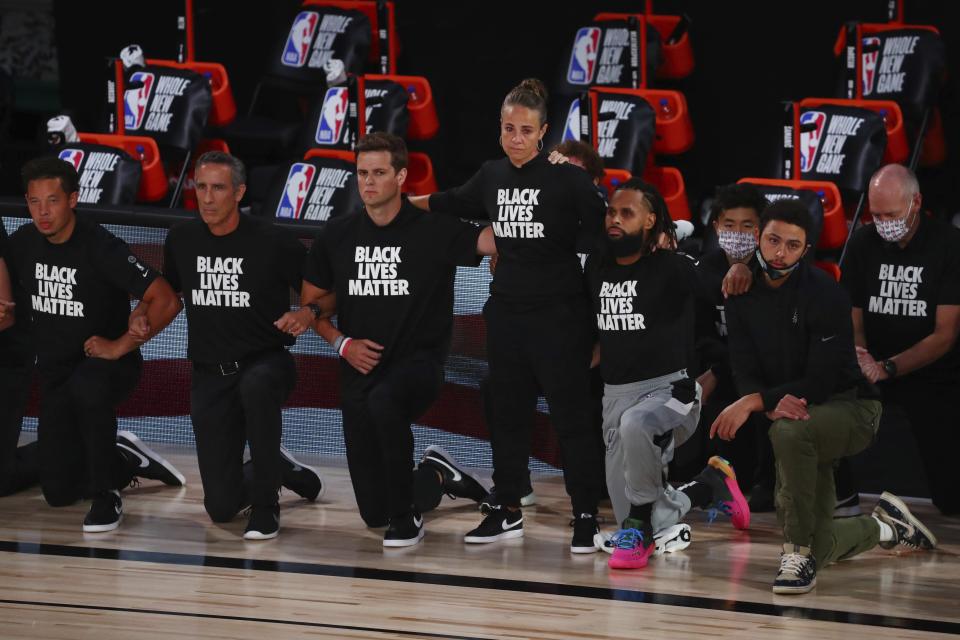 San Antonio Spurs assistant coach Becky Hammon stands as other players and staff kneel in Black Lives Matters shirts before a NBA basketball game against the Sacramento Kings Friday, July 31, 2020, in Lake Buena Vista, Fla. (Kim Klement/Pool Photo via AP)