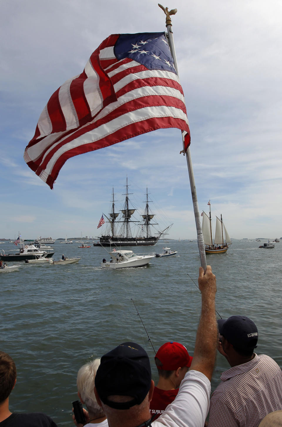 An onlooker waves a colonial era flag as the USS Constitution passes through Boston Harbor in Boston, Sunday, Aug. 19, 2012. The USS Constitution, the U.S. Navy's oldest commissioned war ship, sailed under her own power during the event Sunday for the first time since 1997. The sail was held to commemorate the 200th anniversary of the ship's victory over HMS Guerriere in the War of 1812. (AP Photo/Steven Senne)