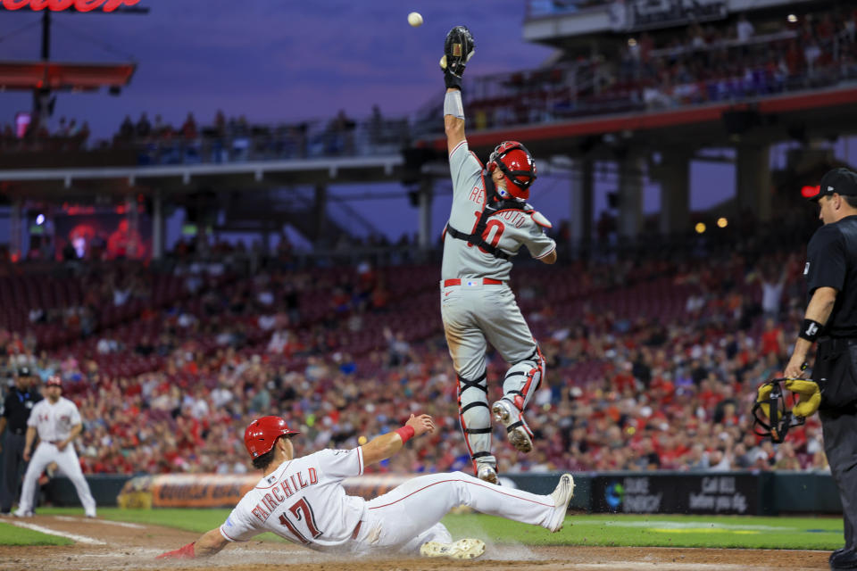 Cincinnati Reds' Stuart Fairchild scores on a single by Wil Myers as Philadelphia Phillies' J.T. Realmuto jumps for the throw during the fifth inning of a baseball game in Cincinnati, Thursday, April 13, 2023. (AP Photo/Aaron Doster)