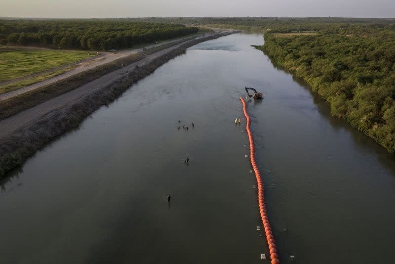 Migrants wade past buoys in Eagle Pass, Texas