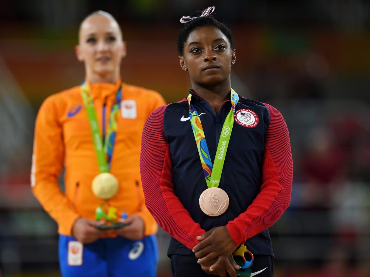 Simone Biles stands with her bronze medal from the 2016 Olympics.