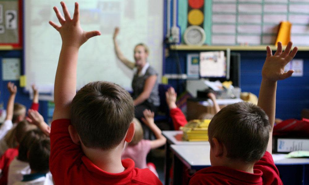 children raising hands to answer question in primary school class