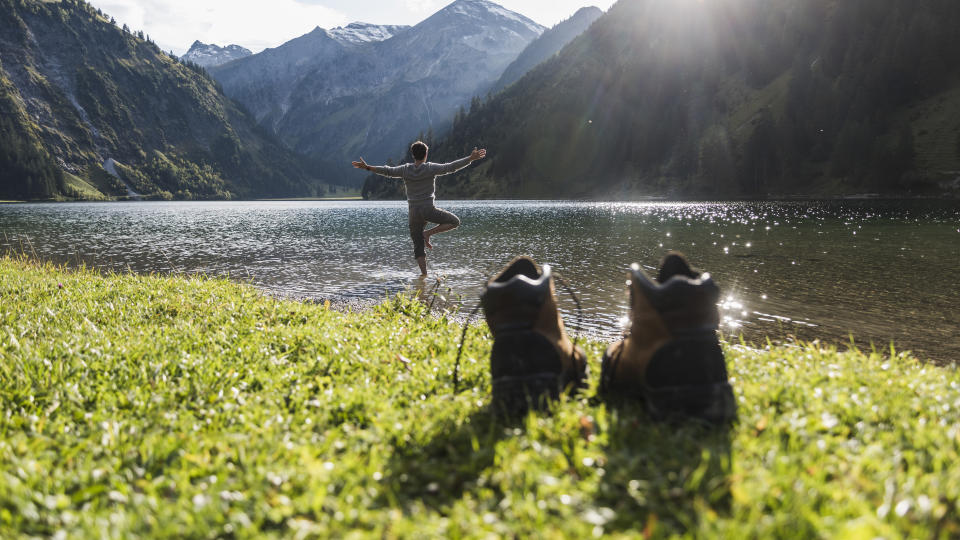 A man doing yoga by a lake with hiking boots in the foreground