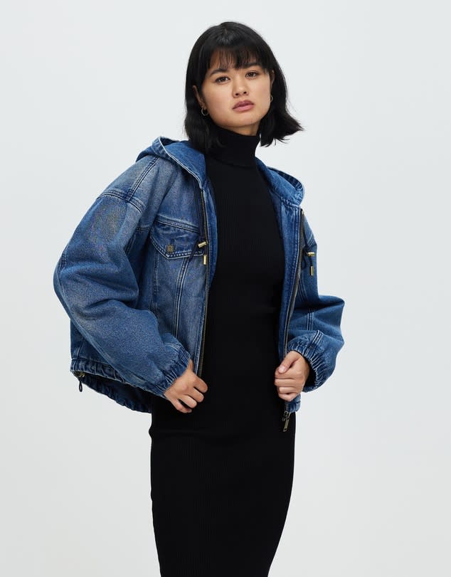 Woman with black bob hairstyle wears a Michael Kors Denim Hooded Bomber Jacket, $435, over black top and pants.