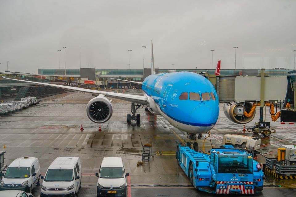 A blue and white plane parked at a gate on a rainy day
