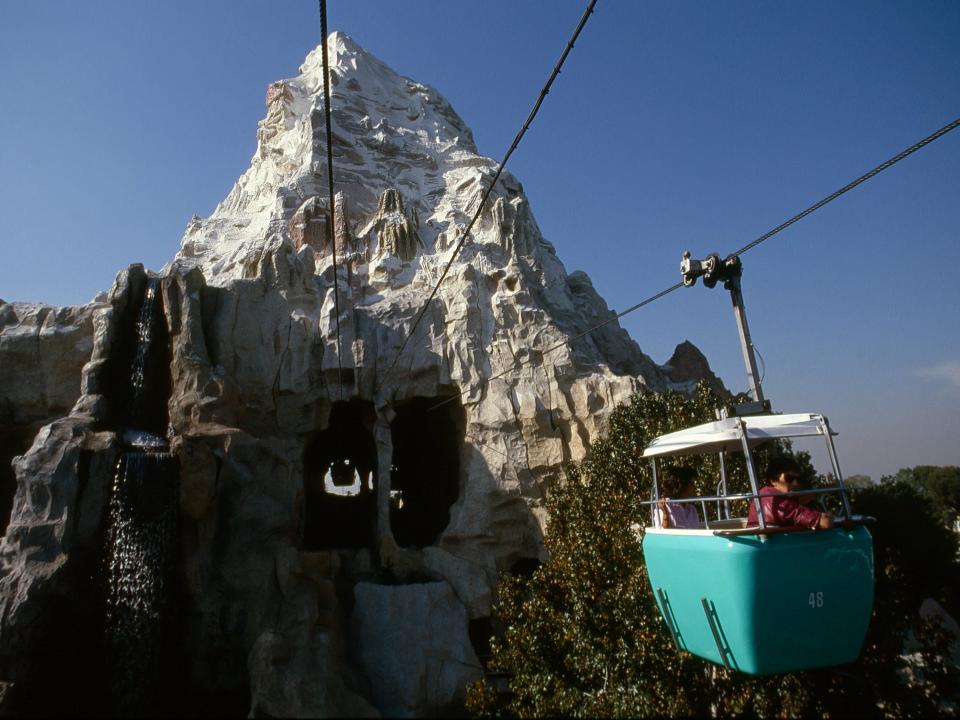 A blue cable car suspended by wires approaching an opening in a rocky mountain structure.