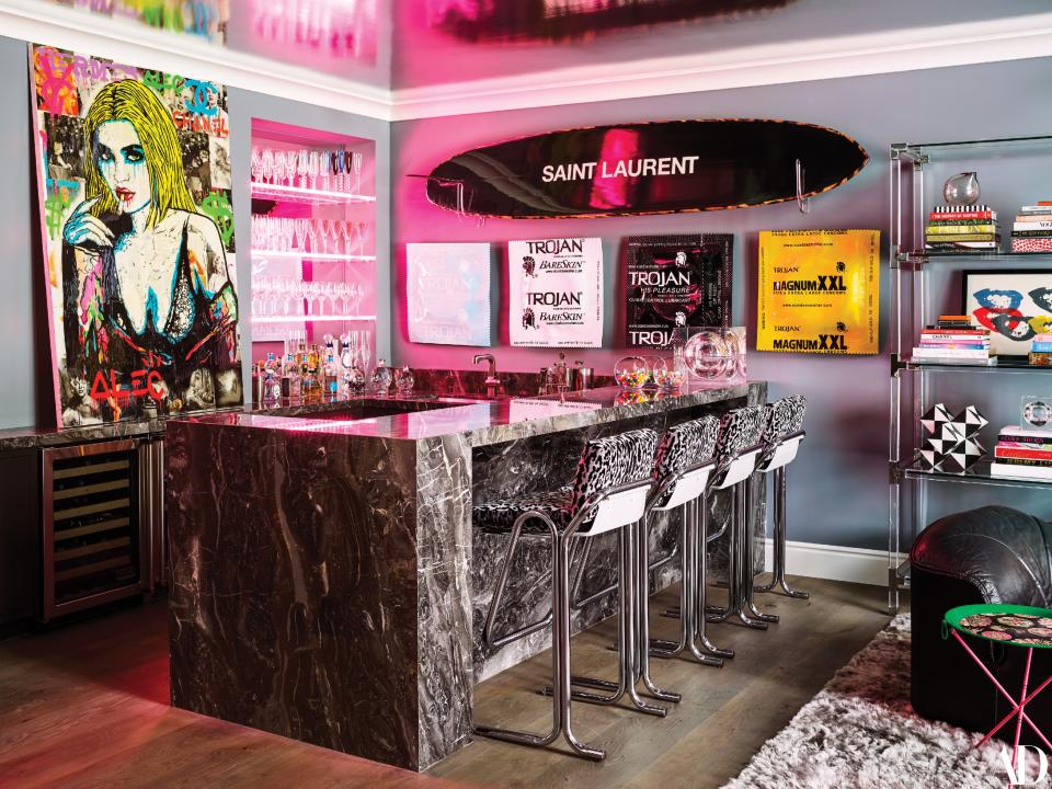 The art-filled bar features a painting by Alec Monopoly (left), condom art by Beau Dunn, and a Saint Laurent surfboard. Vintage Milo Baughman barstools in a Scalamandré print; Kallista sink fittings.