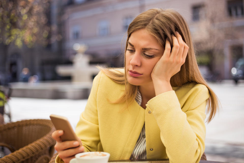 Lonely woman looking at her mobile phone while sitting at the cafe.