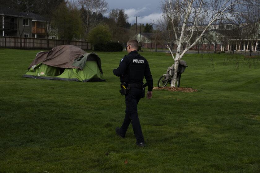 With Fruitdale Elementary School in the background, a Grants Pass police officer walks to check on a homeless person after relatives asked for a welfare check at Fruitdale Park on Saturday, March 23, 2024, in Grants Pass, Ore. (AP Photo/Jenny Kane)