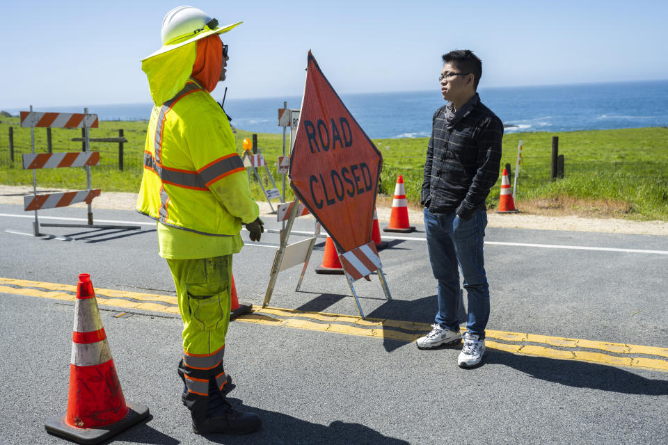 Alejandro Garcia, left, a traffic control technician with Stateside, talks to a tourist at a road closure on Highway 1 near Big Sur, Calif., Monday, April 1, 2024. (AP Photo/Nic Coury)