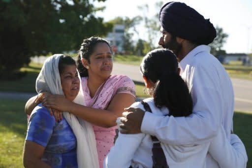 People console each other near the Sikh Temple of Wisconsin where a gunman killed at least six people on August 5. Investigators also released a picture of a second man -- who was white, with short brown hair and a muscular build -- who they described as a "person of interest" and who raised suspicions when he joined crowds viewing the police cordon outside the temple on Sunday