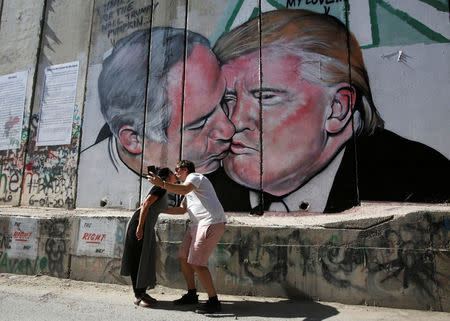 Tourists kiss each other as they stand in front of a mural depicting U.S. President Donald Trump and Israel's Prime Minister Benjamin Netanyahu kisisng each other in the West Bank city of Bethlehem October 29, 2017. REUTERS/Mussa Qawasma