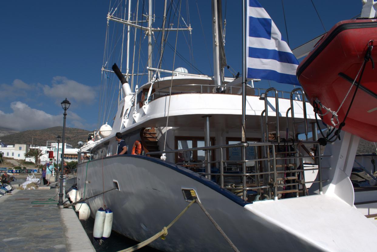 a white ship with Greek flag next to a dock