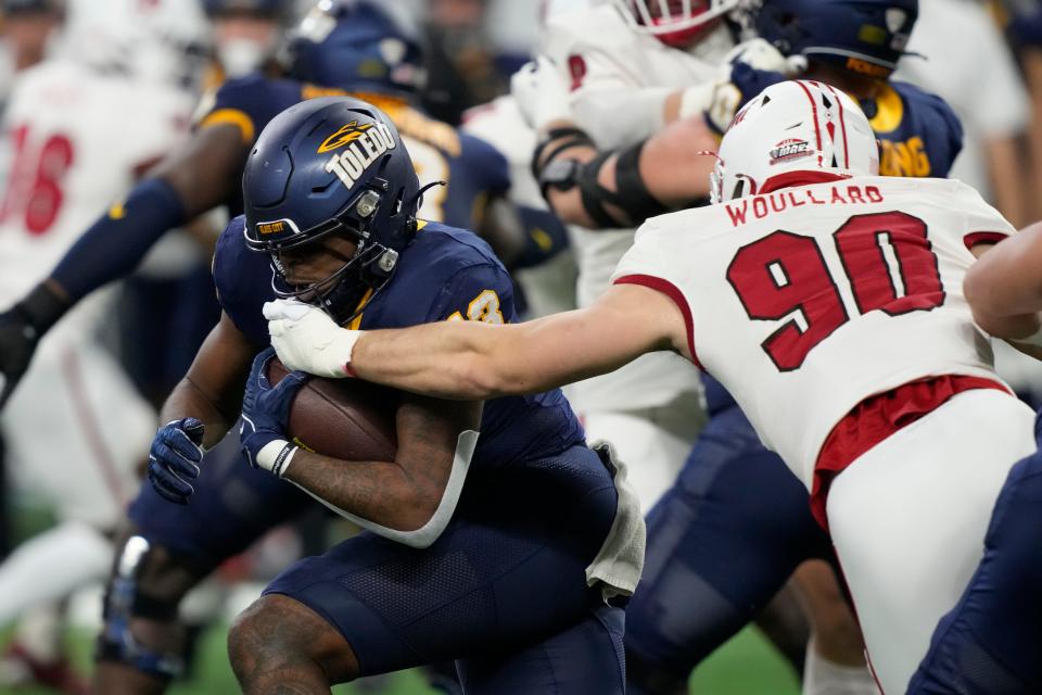 Miami (Ohio) defensive lineman Caiden Woullard (90) reaches for Toledo running back Peny Boone (13) during the first half of the Mid-American Conference Championship Game, Saturday, Dec. 2, 2023, in Detroit.