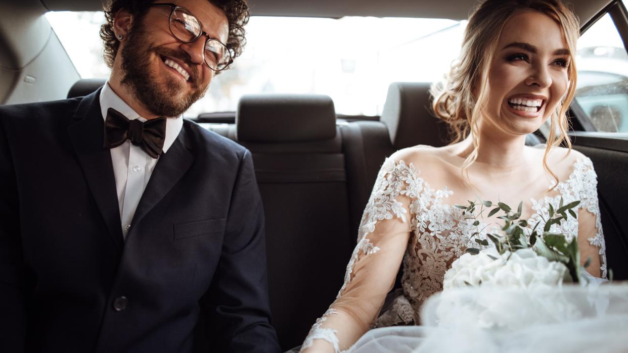 Newlyweds holding hands in the backseat.