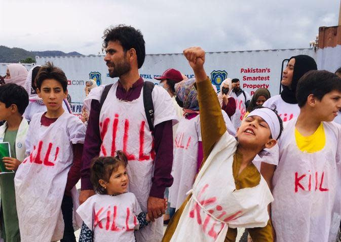 Fahim Baraki stands with his daughter as his son gestures during a protest in Islamabad, Pakistan, June 20, 2022, held by his family and hundreds of other Afghan refugees demanding legal status as asylum seekers. The word 