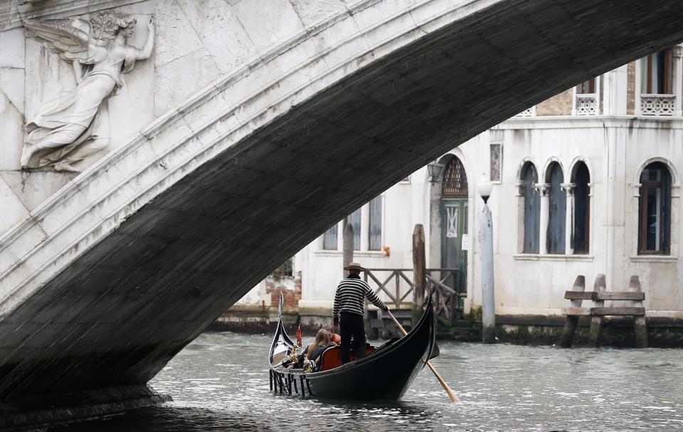 A gondolier rows past the Rialto bridge in Venice