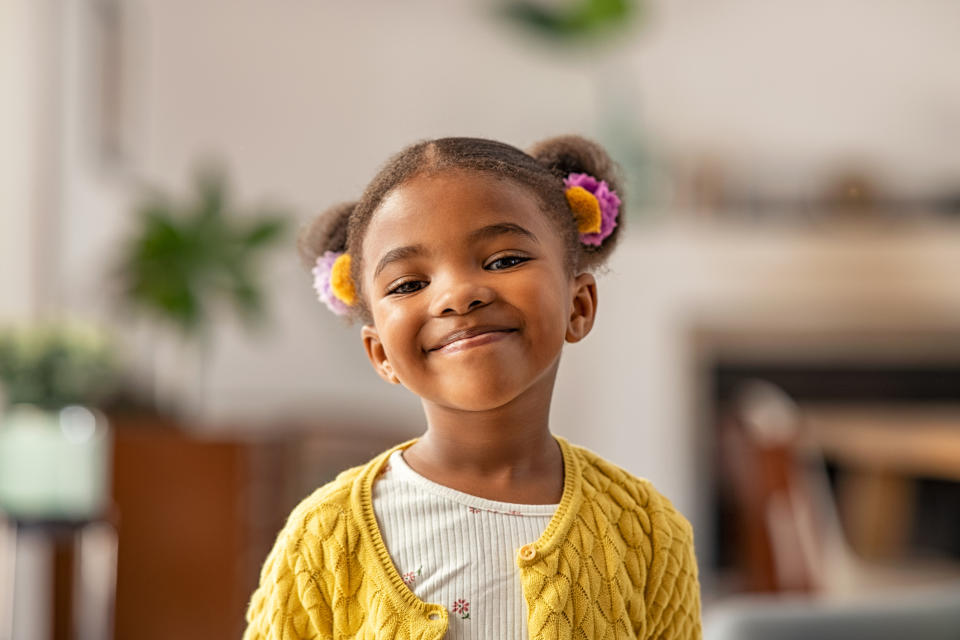 Young girl smiling with pigtails, wearing a knitted cardigan indoors