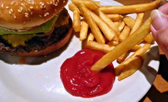 A person dips French fries in ketchup, next to a burger