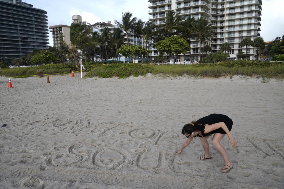 Faydah Bushnaq, of Sterling, Va., writes "Pray for their Souls" in the sand outside of a 12-story beachfront condo building which partially collapsed, Friday, June 25, 2021, in the Surfside area of Miami. Bushnaq is vacationing and stopped to write in the sand. The apartment building partially collapsed on Thursday. (AP Photo/Lynne Sladky)