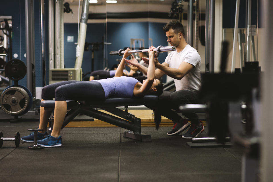 Young woman exercising with personal trainer in a gym. Coach is next to her and he is motivating her and helping her.