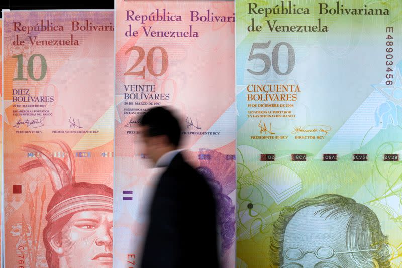 FILE PHOTO: A man walks past big samples of Venezuelan bank notes at the Central Bank headquarters in Caracas