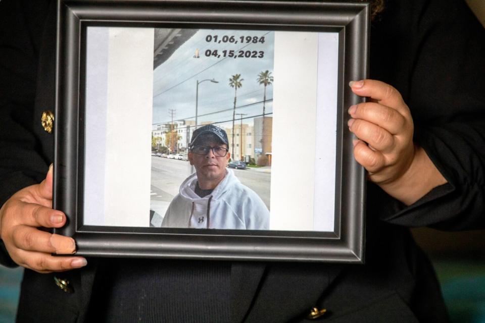 A midsection frame of a person holding a framed photograph of a man wearing glasses, a cap and a hooded sweatshirt.